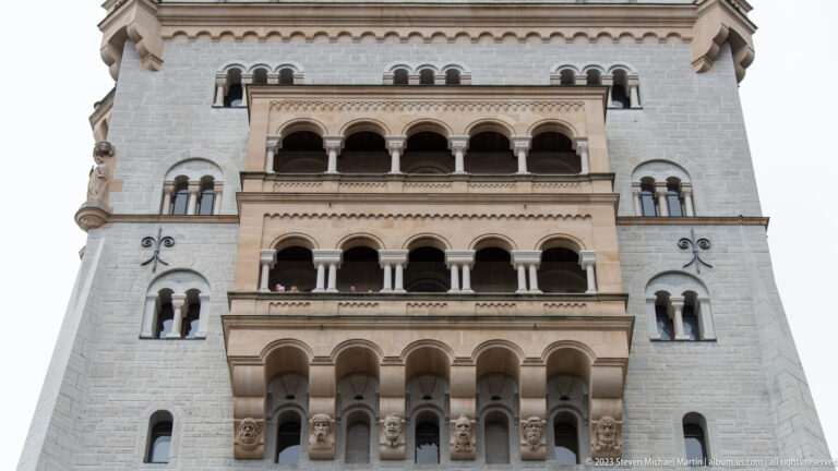 Stacked rows of round-arched loggias and columns on the pale stone facade of Neuschwanstein Castle.