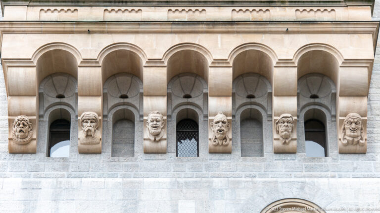 Carved grotesque heads projecting between round arches on the pale stone facade of Neuschwanstein Castle.