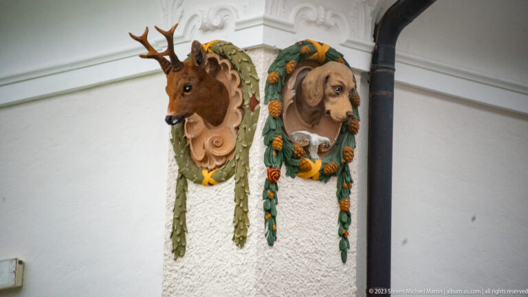 Decorative deer and hound heads mounted in ornate foliage frames on an exterior corner of Hohenschwangau Castle.