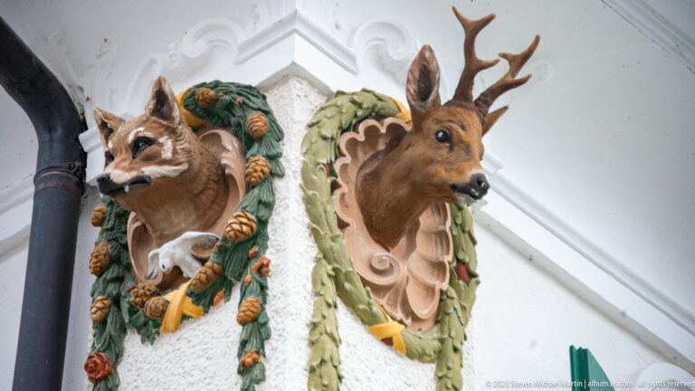 Fox-like and antlered deer heads projecting from ornate green and tan mounts on Hohenschwangau Castle.