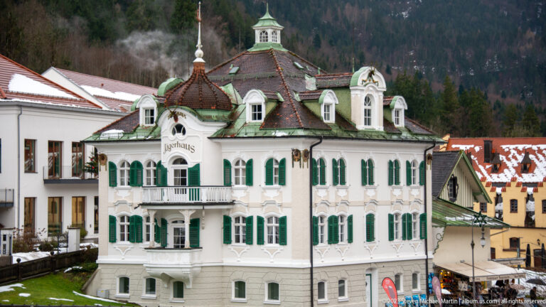 White Jägerhaus with green shutters, curved dormers, balcony, and roof lantern in the snowy Hohenschwangau district.