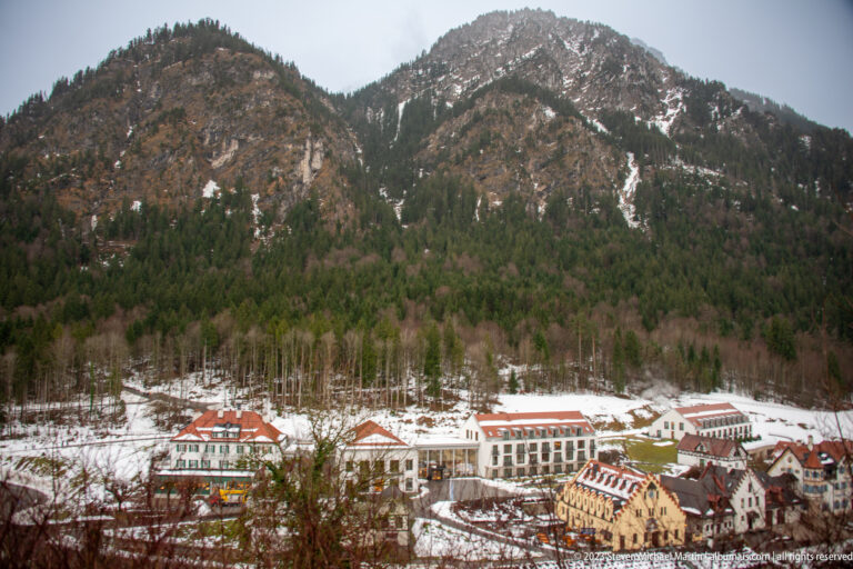 Snowy Hohenschwangau settlement beneath a steep forested mountain with scattered snow on its upper slopes.
