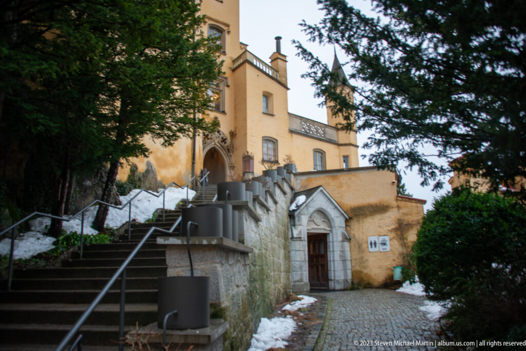 Stone steps and railings beside Hohenschwangau Castle leading to a small pointed-arched doorway in the ochre wall.