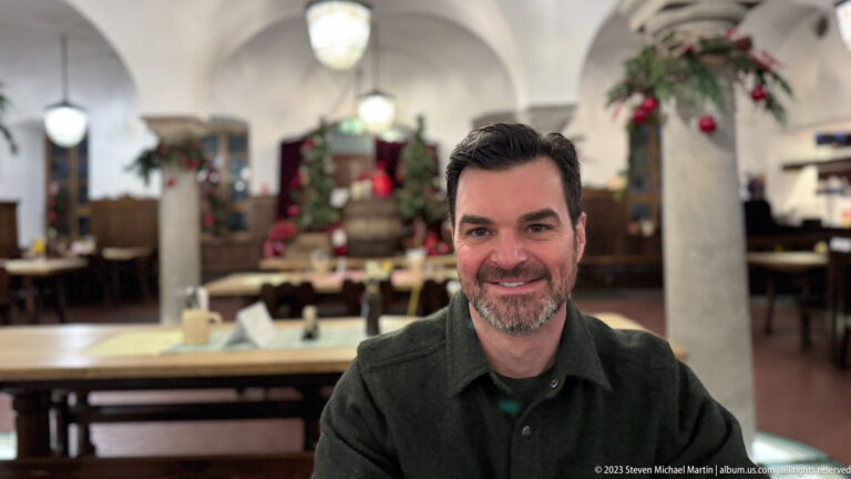 Smiling male visitor seated in a restaurant with columns, wooden tables, and Christmas decorations in the background.