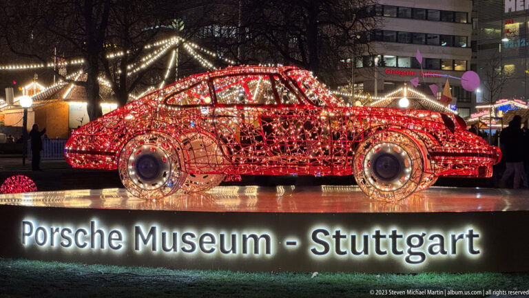Red illuminated wireframe sports car above a glowing “Porsche Museum – Stuttgart” sign at night.