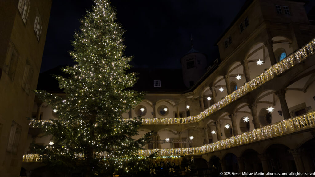 Tall illuminated Christmas tree inside the arcaded Renaissance courtyard of Stuttgart’s Altes Schloss at night.