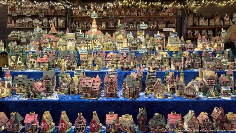 Dense display of colorful miniature houses, churches, towers, and shops arranged in rows beneath warm Christmas lights.
