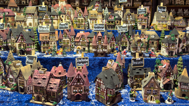 Close view of colorful miniature half-timbered houses, towers, and civic buildings with small labels arranged on blue fabric.