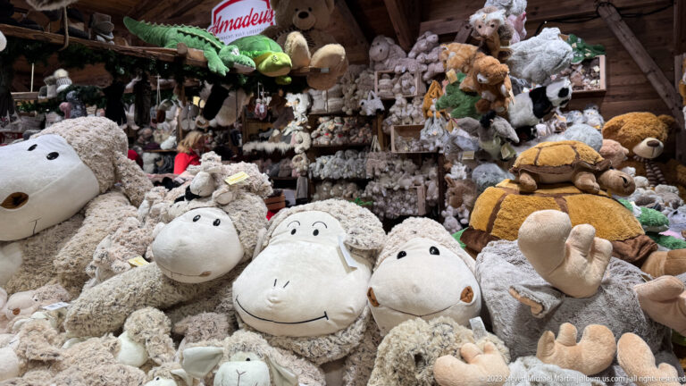 Christmas-market stall packed with plush animals, dominated by large white stuffed sheep in the foreground.