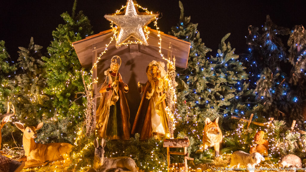 Illuminated Nativity scene with Mary, Joseph, animal figures, fir branches, and a glowing star at Stuttgart’s Christmas market.