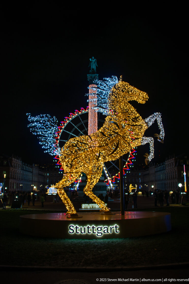 Golden illuminated winged horse sculpture with blue light forms behind it and the word Stuttgart below.