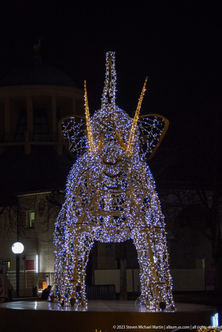 Large symmetrical crown-like holiday light sculpture outlined with cool white bulbs against a dark Stuttgart street.