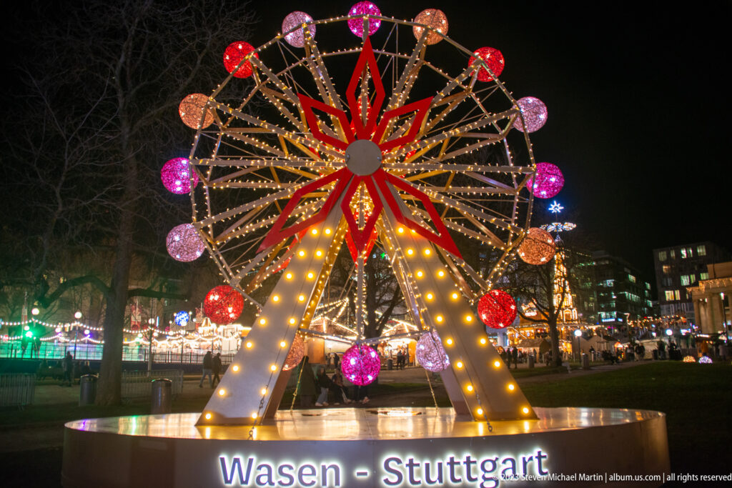Decorative Ferris-wheel-shaped light installation with colorful bulbs and the illuminated words Wasen - Stuttgart.