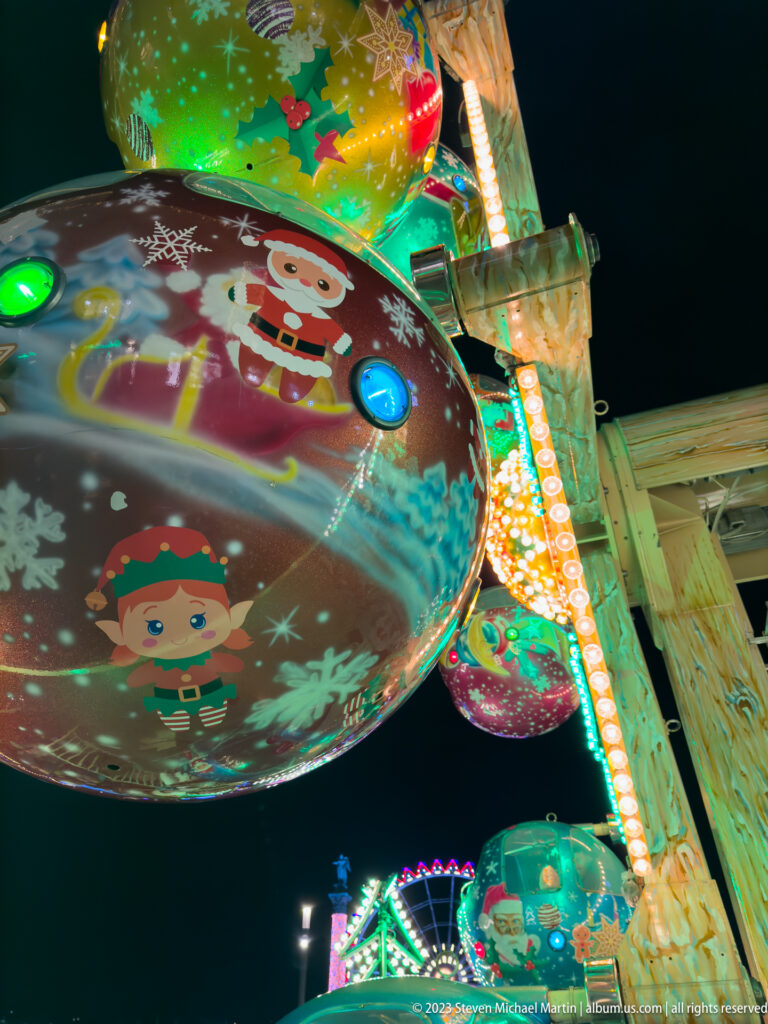 Low-angle view of a round amusement-ride canopy painted with cartoon Christmas figures, snowflakes, and colored lights.