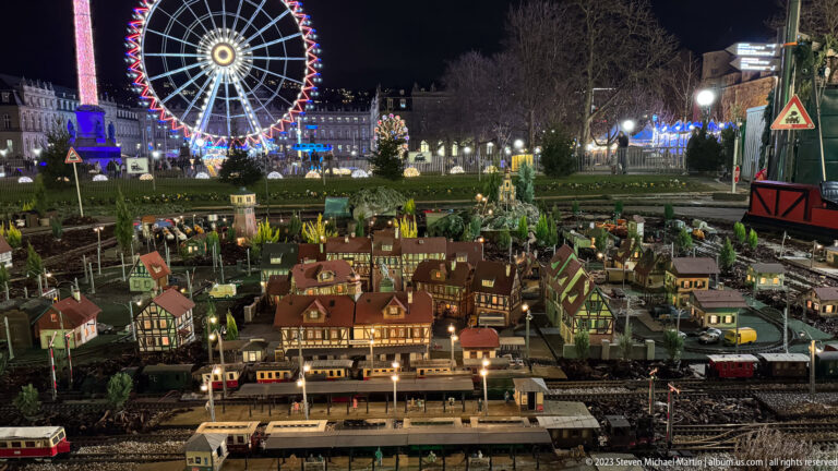 Large miniature railway display with model trains, station buildings, houses, roads, and a Ferris wheel in the background.