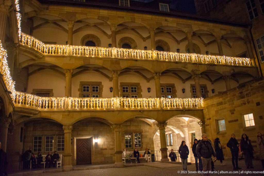 Two-story arcaded courtyard of Stuttgart’s Altes Schloss outlined with warm Christmas lights at night.