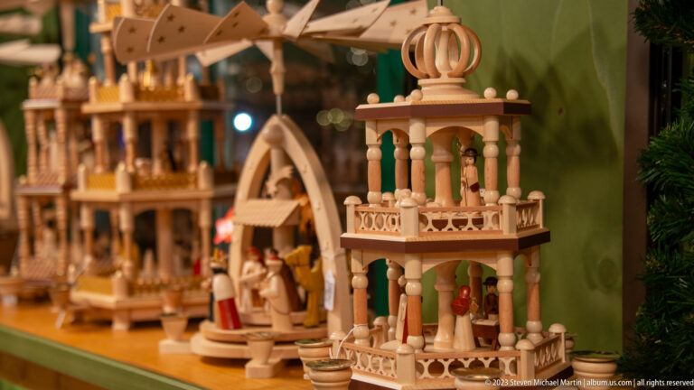 Wooden Christmas pyramid with miniature figures, railings, and turned columns displayed among other traditional decorations.