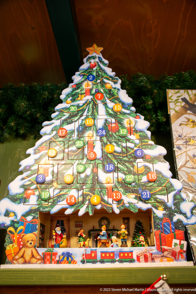 Christmas-tree-shaped wooden Advent calendar with colorful numbered doors and small toy figures along the base.
