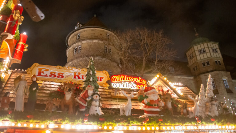 Decorated Christmas market food stall beneath the large round stone tower of Stuttgart’s Altes Schloss at night.