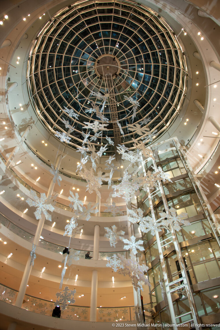 Modern circular shopping atrium with a glass roof and many white seasonal ornaments suspended through the central void.
