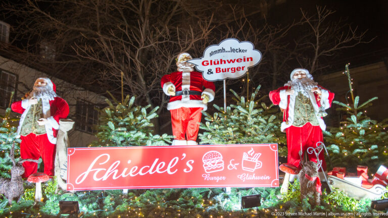 Three Santa figures and fir trees decorate Schiedel’s Christmas market stall, with signs for Glühwein and burgers.