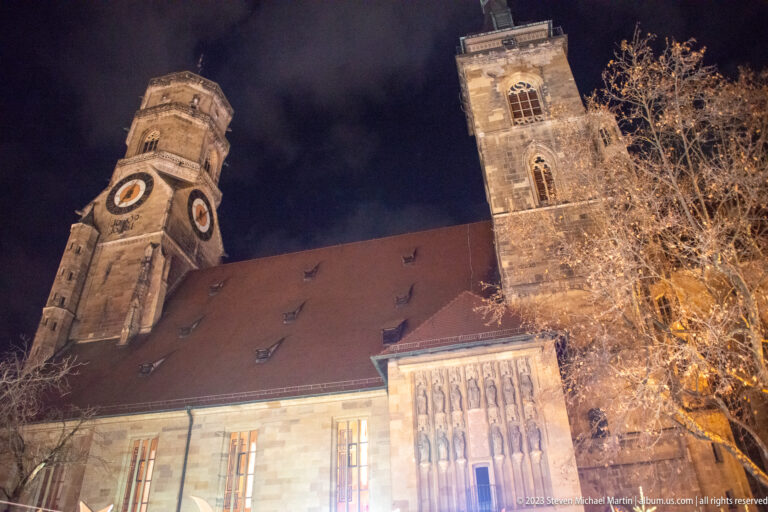 Stiftskirche at night with its clock tower, taller square tower, red-tiled roof, and large Gothic window.