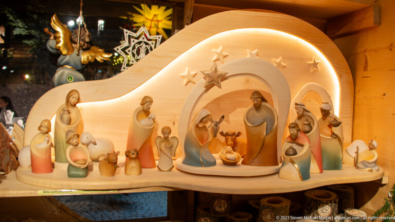 Carved wooden Nativity with Mary, Joseph, infant Jesus, shepherds, animals, and stars beneath a glowing arch.