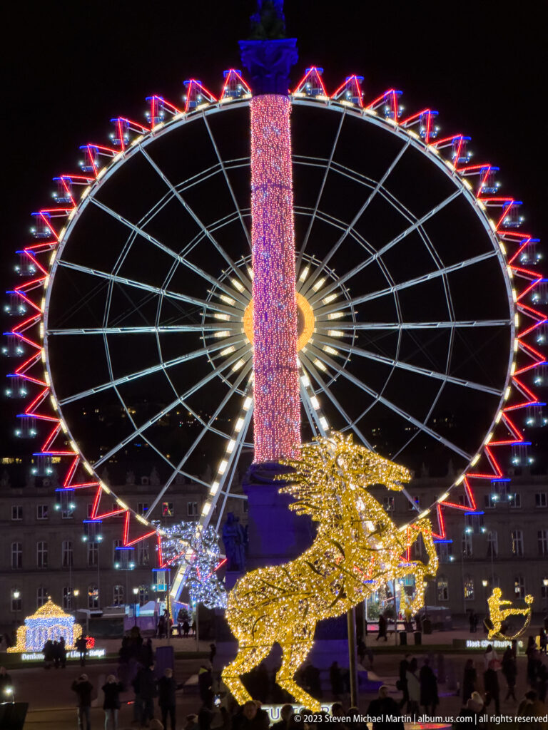 Ferris wheel behind the Jubilee Column on Schlossplatz, with a glowing leaping animal sculpture in the foreground.