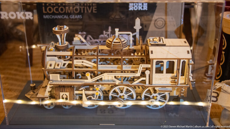 Intricate wooden locomotive model with wheels, rods, and cab details displayed behind reflective glass.