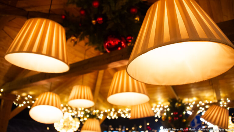 Several glowing pleated conical lampshades hanging above fairy lights and evergreen decorations.