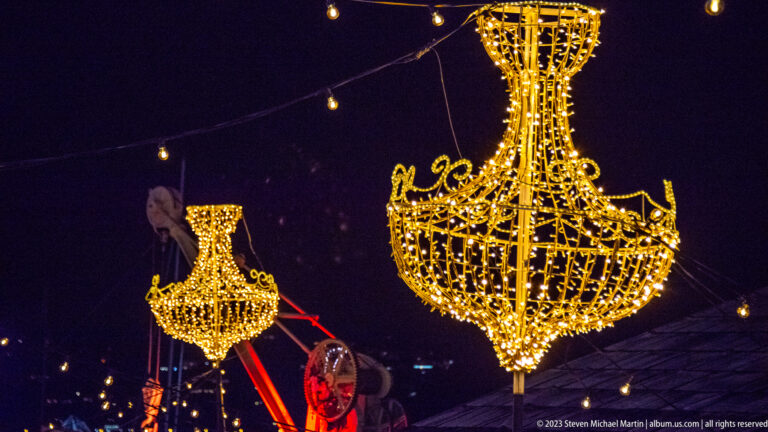 Large chandelier-shaped golden light decorations suspended over a city street at night.