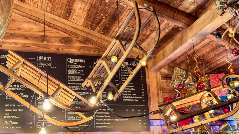 Wooden sleds suspended from timber rafters in front of black drink menus and hanging bulbs.
