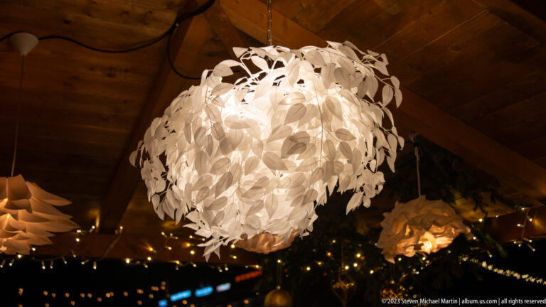 Large glowing spherical pendant made of overlapping white leaf-like pieces under timber rafters.