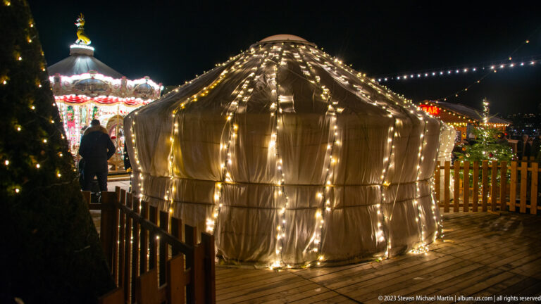Small translucent arched shelter outlined with warm string lights beside a wooden railing at night.