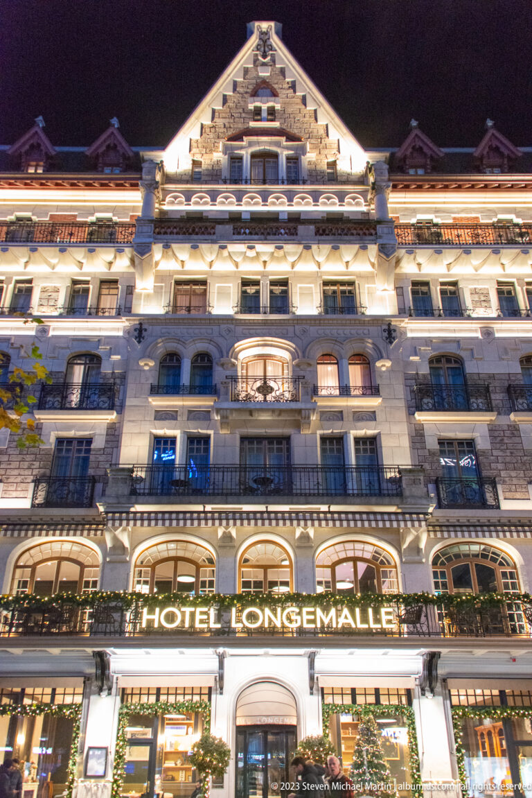 Low-angle nighttime view of the multi-story Hôtel Longemalle façade with balconies, arched windows, and illuminated roofline.