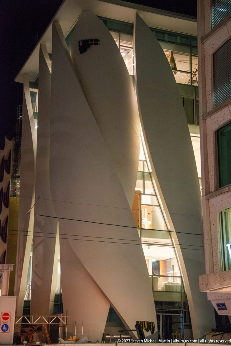 Large curved white architectural fins framing glass windows on a contemporary building at night.