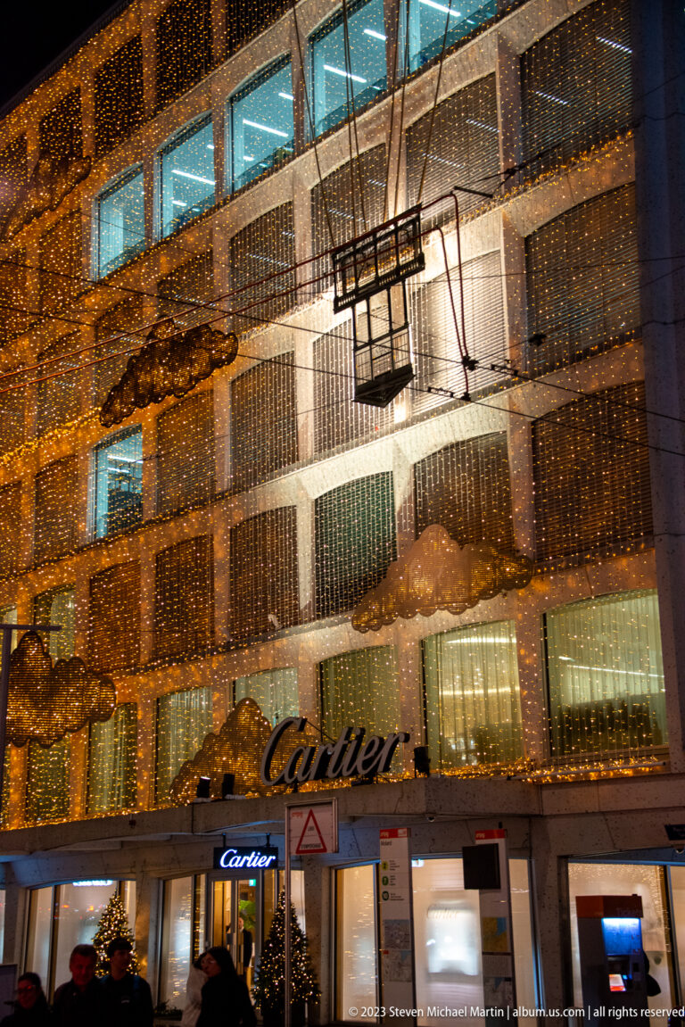 Cartier storefront beneath a multi-story façade covered in dense golden lights and dark linear decorations.
