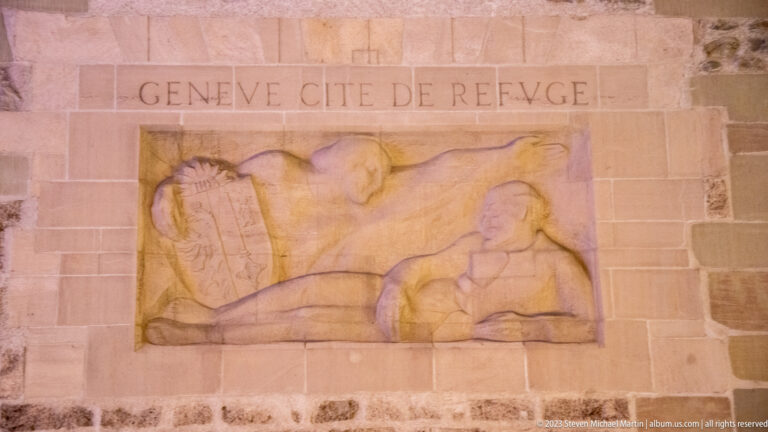 Stone relief inscribed “GENÈVE CITÉ DE REFUGE” above two reclining carved human figures.