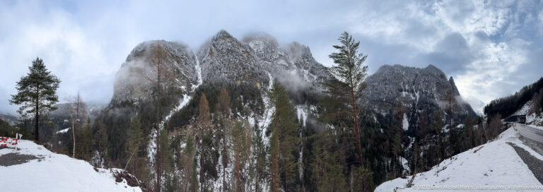 Jagged vertical rock towers above snowy conifers, with cloud wrapping around the upper cliffs.