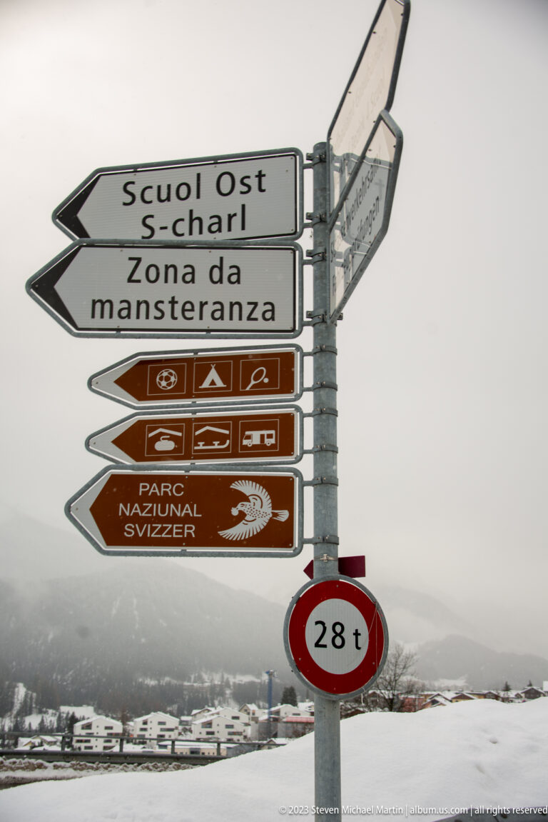 Road sign cluster pointing to Scuol Ost, S-charl, and Parc Naziunal Svizzer above a 28-ton restriction sign.