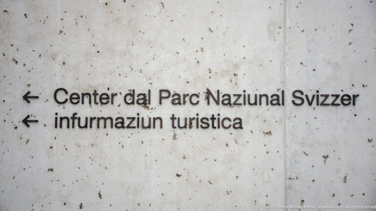 Concrete wall with Romansh arrows and text for 'Center dal Parc Naziunal Svizzer' and tourist information.