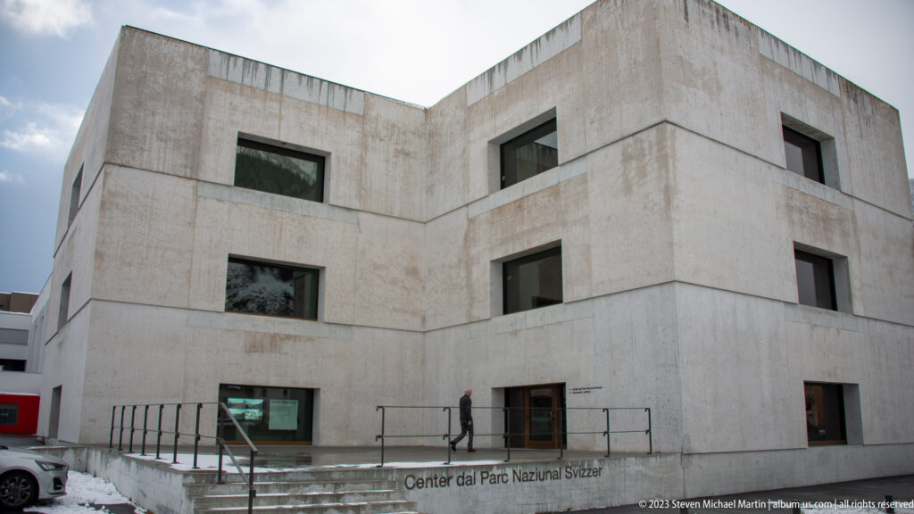 Modern pale-concrete visitor center with deep rectangular windows, angular volumes, and entrance steps.