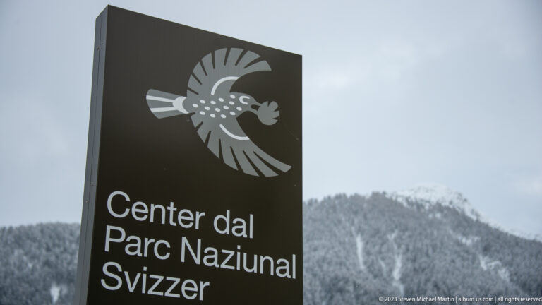 Black sign reading 'Center dal Parc Naziunal Svizzer' beneath a stylized white bird emblem.