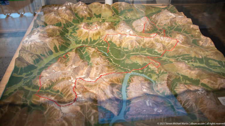 Three-dimensional alpine relief map with forests, peaks, valleys, and a red boundary line marking the park area.