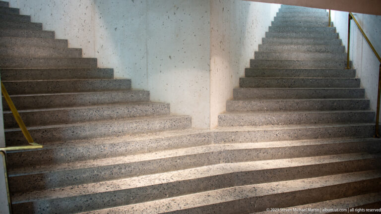 Two speckled concrete stair flights rising on either side of a central wall with slim handrails.