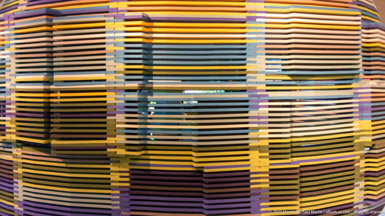 Close view of a visitor-center installation built from tightly layered horizontal slats in many muted colors.