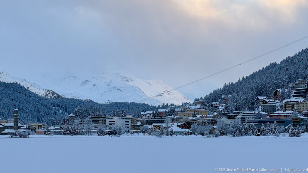 St. Moritz stretches along the far edge of a frozen lake, backed by forested slopes and snowy mountains.