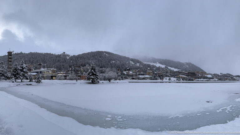 Frozen Lake St. Moritz fills the foreground, with the town and wooded hills stretching across the distant shore.