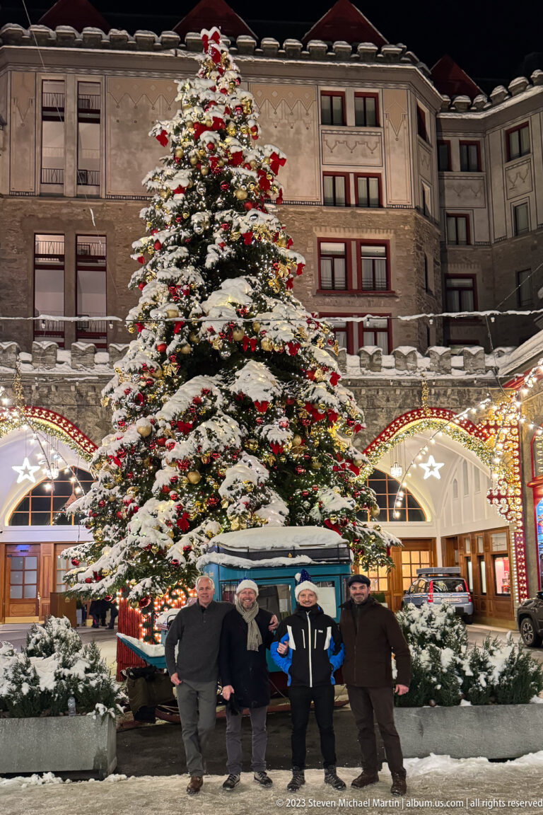 Large decorated Christmas tree outside a grand hotel, with four men and a blue vehicle marked Palace Hotel at its base.