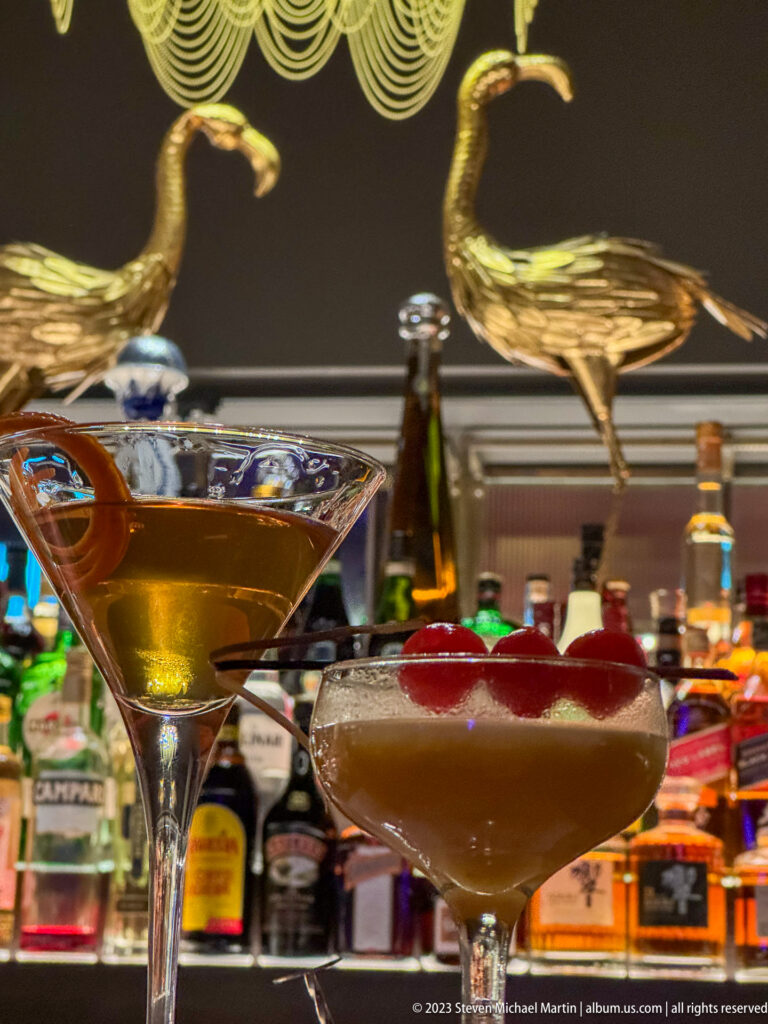 Two cocktails side by side: an amber drink with curled citrus peel and a frothy drink topped with red fruit.